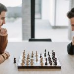 Two adults deeply engaged in a strategic chess match on a wooden table indoors.