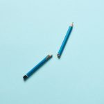 A conceptual image of a broken blue pencil on a light blue surface, symbolizing creativity and challenges.