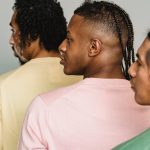 Back view of diverse male models in trendy clothes standing close and looking away against gray background